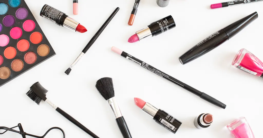 Een rij lippenstiften, enkele kwasten en een palet oogschaduw op wit